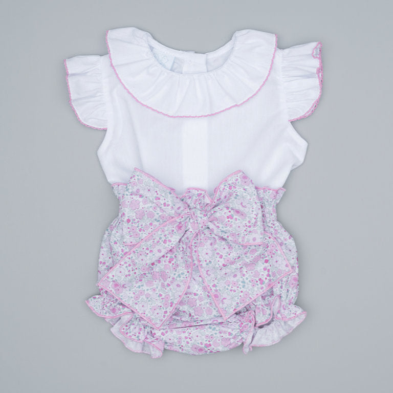 Baby romper with floral design and ruffled white top on a pink, floral background