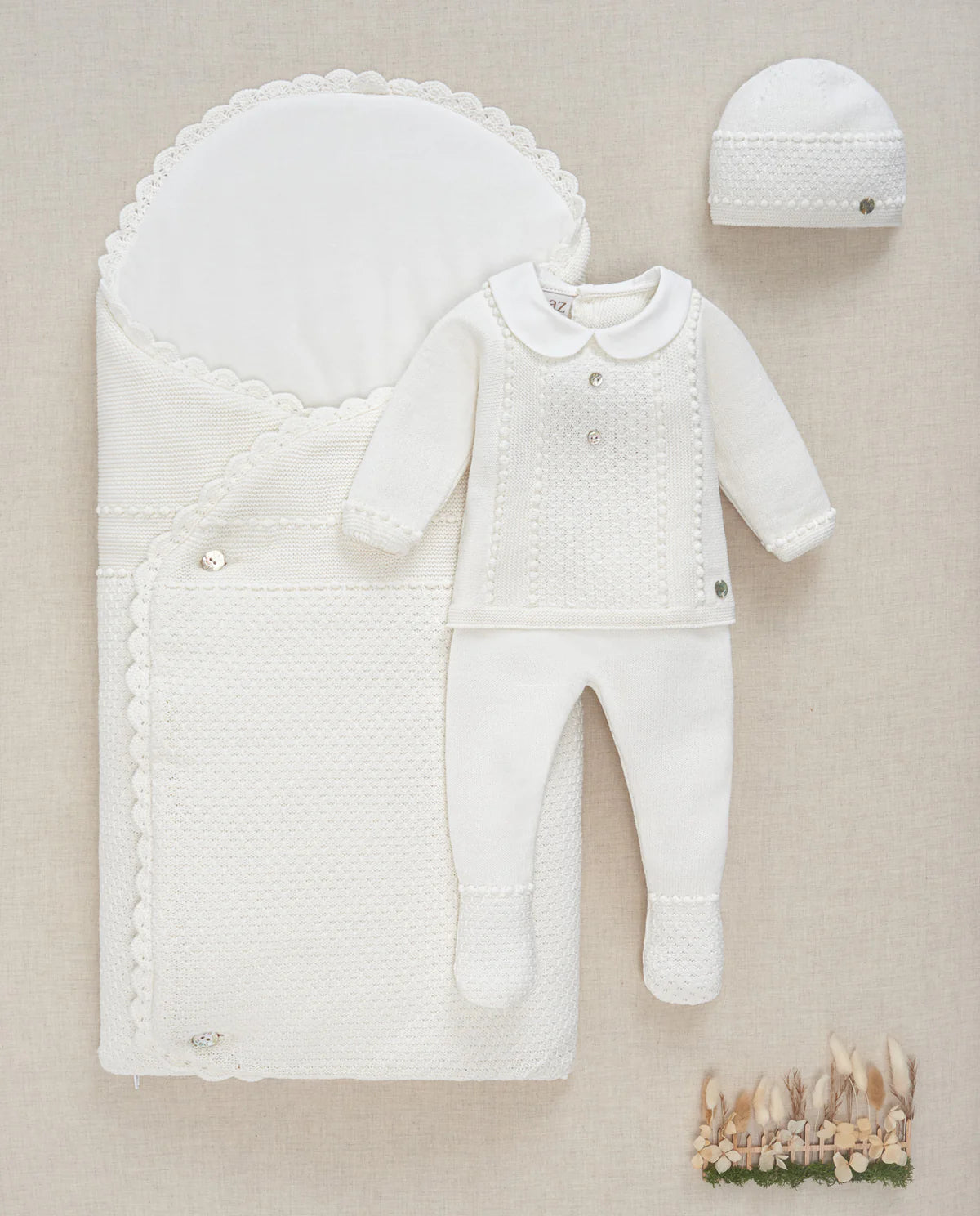 White baby outfit with hat and baby nest on a beige background