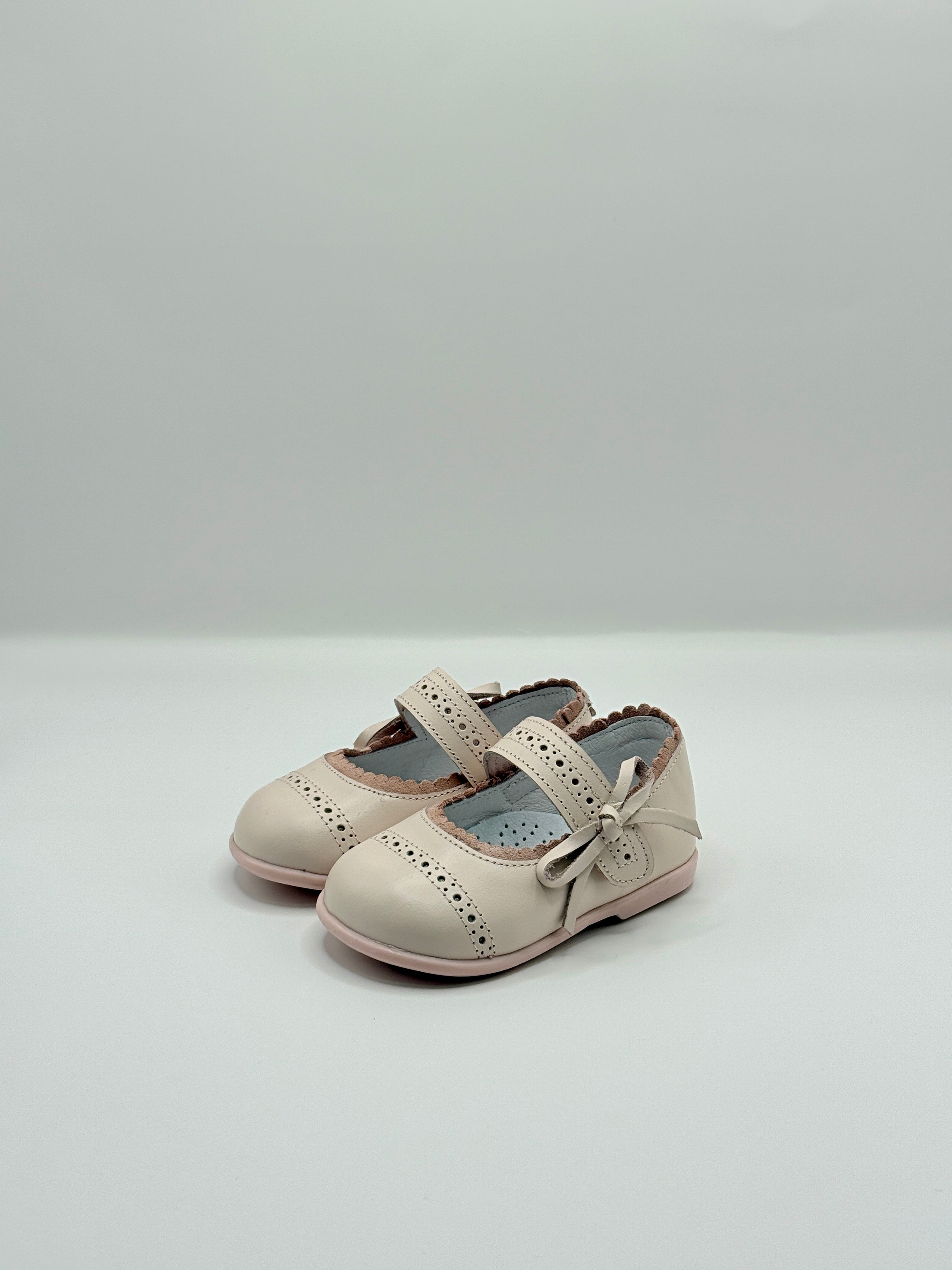 Pair of beige children's shoes with a bow on a light gray background