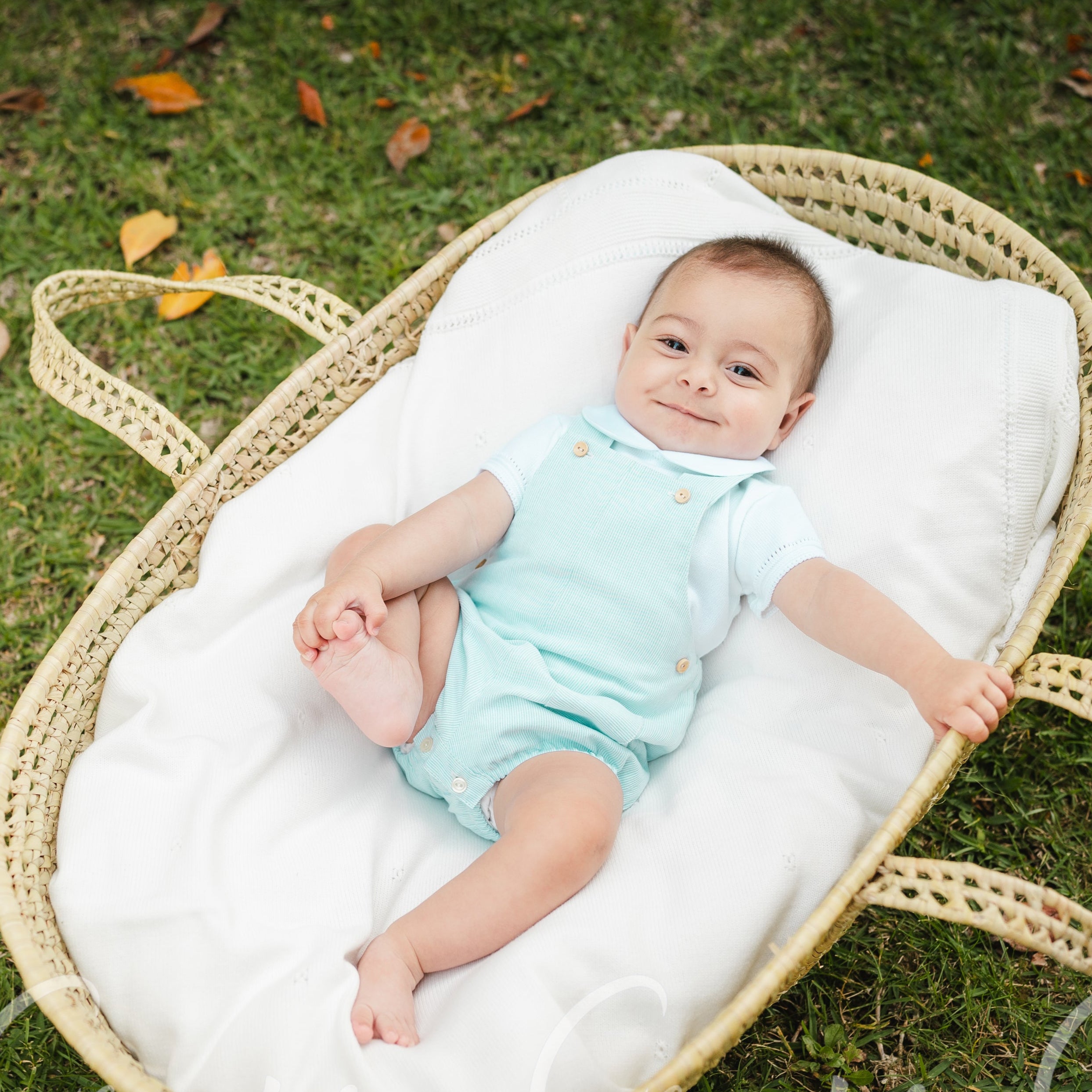 Baby lying in a wicker basket on grass with 'Granlei' branding.